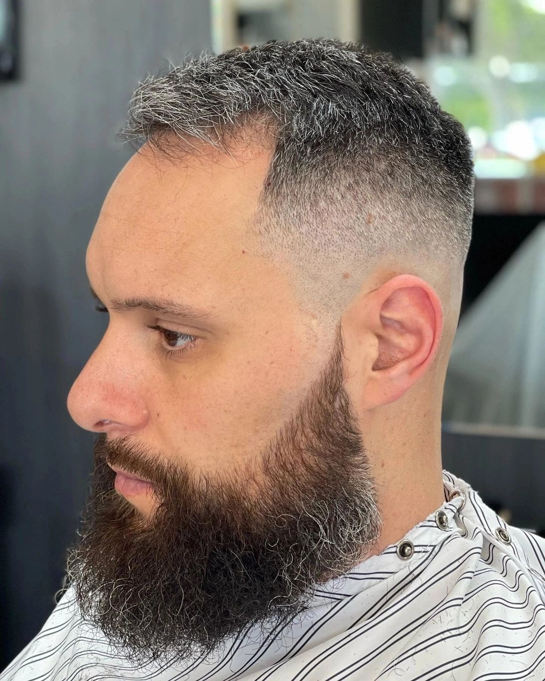 Side profile of a client with a high skin fade blended into a full beard.