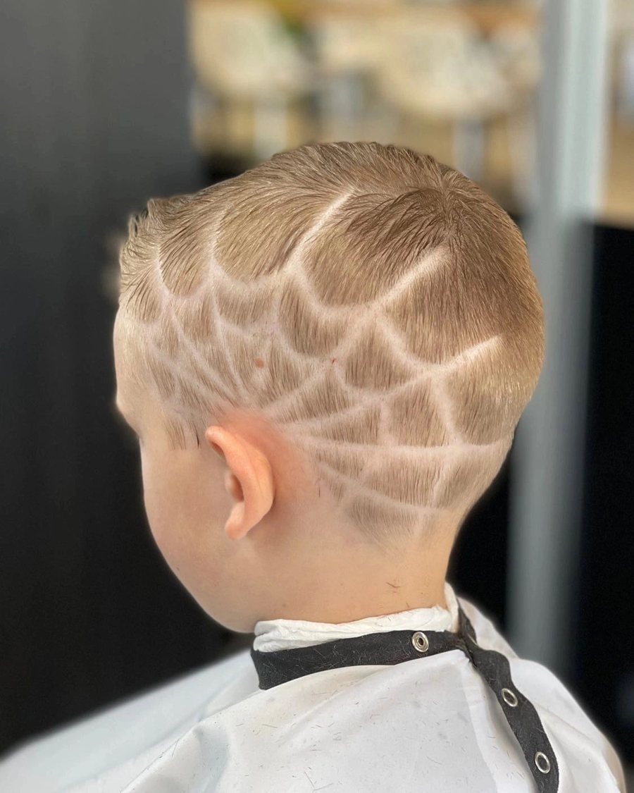 Back of a boy's head with a spider web pattern shaved into the fade.