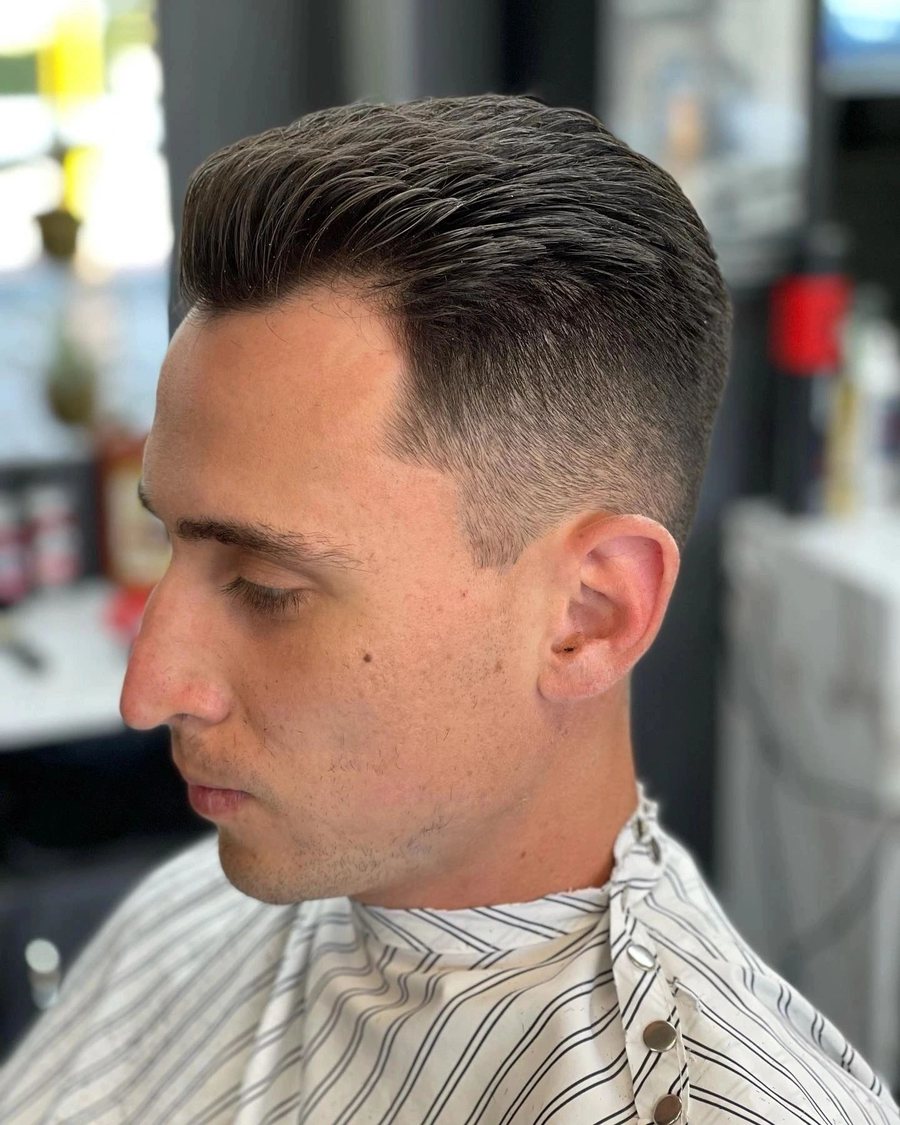 Side profile of a man with dark hair swept back above a high skin fade.